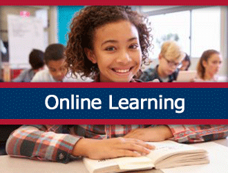 A girl at her desk smiling at the camera while reading a book in an elementary classroom. A ribbon that says 